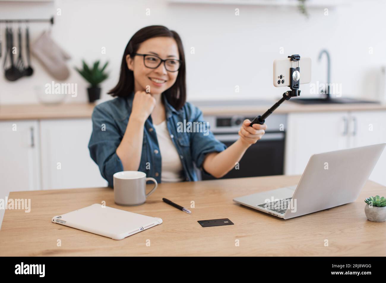 Eine energiegeladene Frau, die sich auf einem Selfie-Stick mit einem modernen Smartphone für einen persönlichen Blog filmt. Positive asiatische Frau in Brillen, die Online-Kurse aufnehmen wh Stockfoto