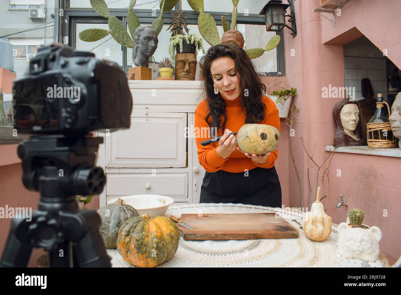 kaukasische Erwachsene Frau in orangefarbener Kleidung und schwarzer Hose mit ihrer Digitalkamera lächelnde Anleitung für halloween Nacht, Konzept der Tutorials, tec Stockfoto