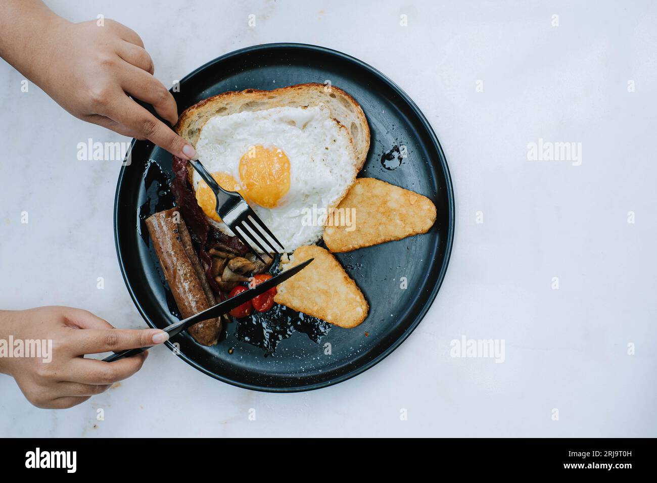 Flache Lage oder Draufsicht und selektiver Fokusschuss von den Händen zerteilt den Sauerteig auf einem Teller voll englisches Braten Frühstücksmenü auf isoliertem weißem bac Stockfoto