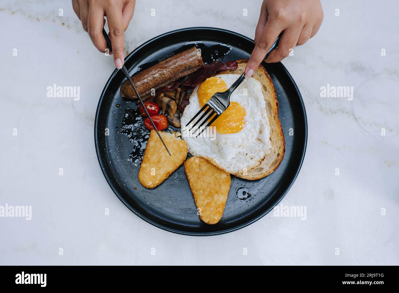 Flache Lage oder Draufsicht und selektiver Fokusschuss von den Händen zerteilt den Sauerteig auf einem Teller voll englisches Braten Frühstücksmenü auf isoliertem weißem bac Stockfoto