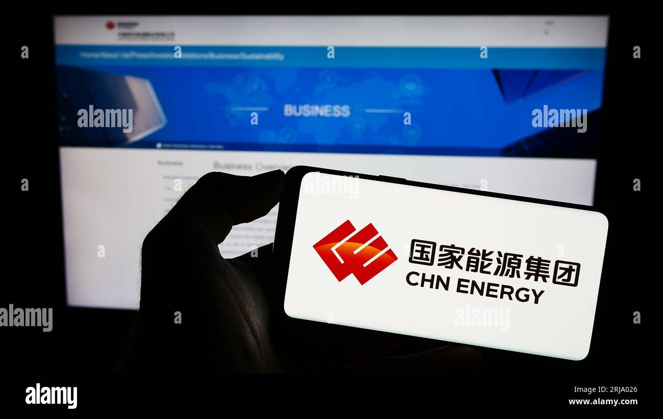 Person, die ein Mobiltelefon mit dem Logo der Firma China Energy Investment Corporation auf dem Bildschirm vor der Webseite hält. Konzentrieren Sie sich auf das Display des Telefons. Stockfoto