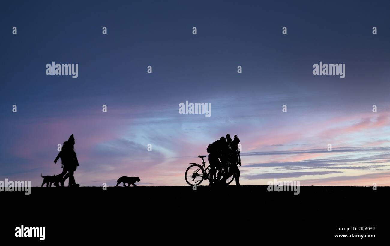 Silhoutte von Menschen, die mit Hunden und Fahrrädern mit Sonnenuntergang laufen Stockfoto