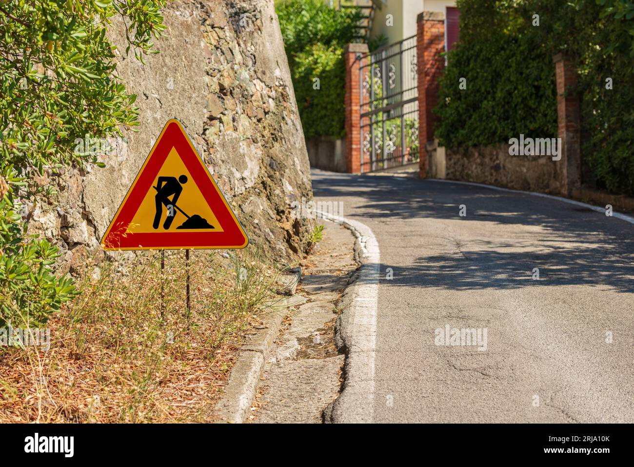 Dreieckiges orangefarbenes, rotes und schwarzes Straßenschild von Männern bei der Arbeit oder bei der Arbeit, an der Seite einer Straße, die in Instandhaltung ist (schlechter Zustand). Italien, Europa. Stockfoto