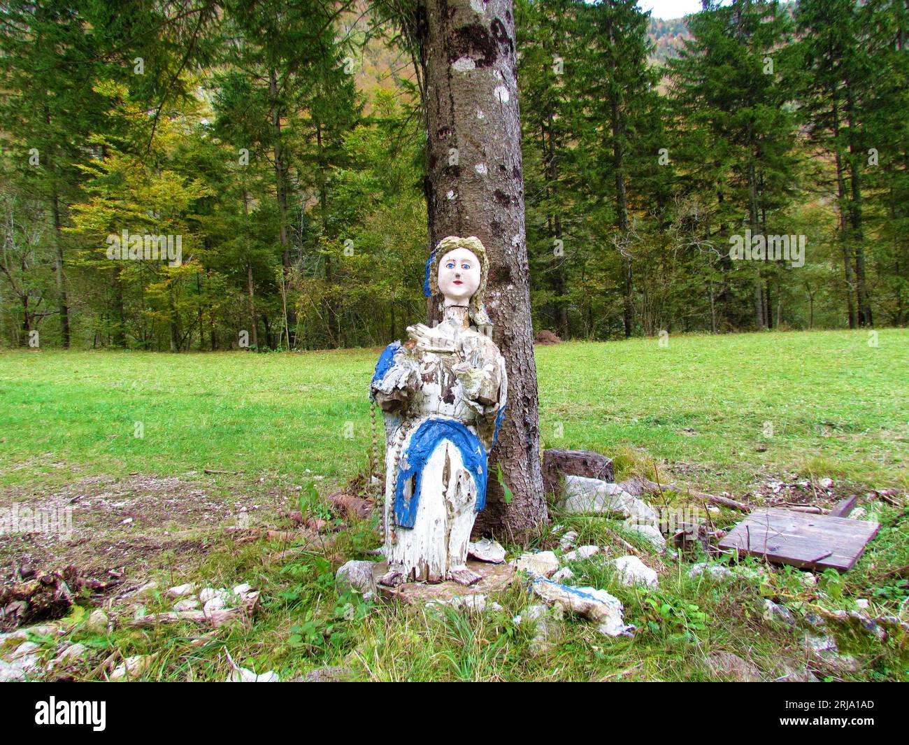 Alte gruselige, abgenutzte, weiße und blaue Puppe, die auf einem Baum lehnte Stockfoto