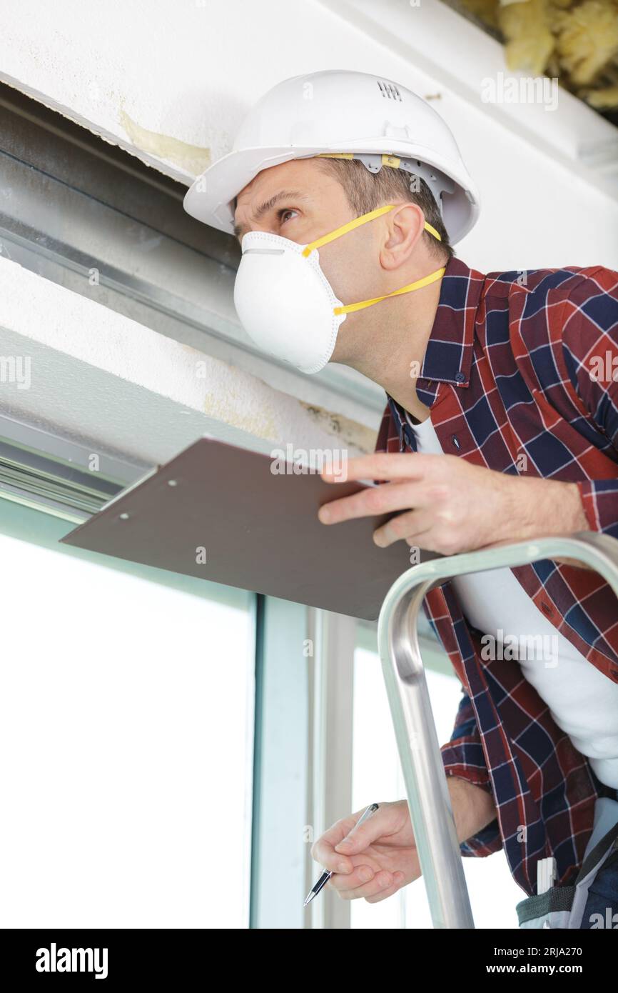 Männlicher Baumeister, der eine Maske trägt, die den Fensterrahmen sichert Stockfoto