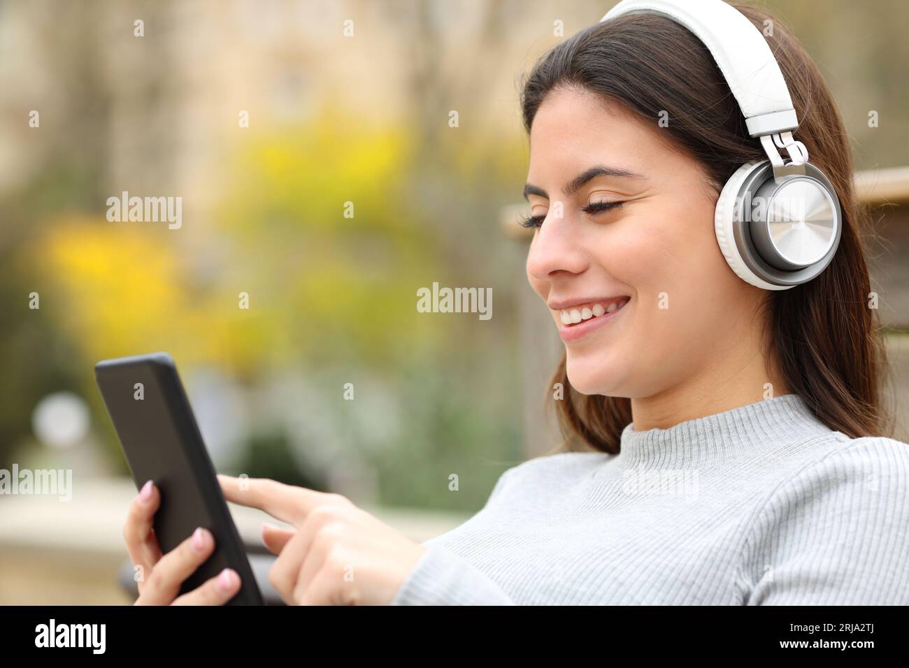 Fröhlicher Teenager, der Musik hört, mit Kopfhörern und Smartphone im Park Stockfoto