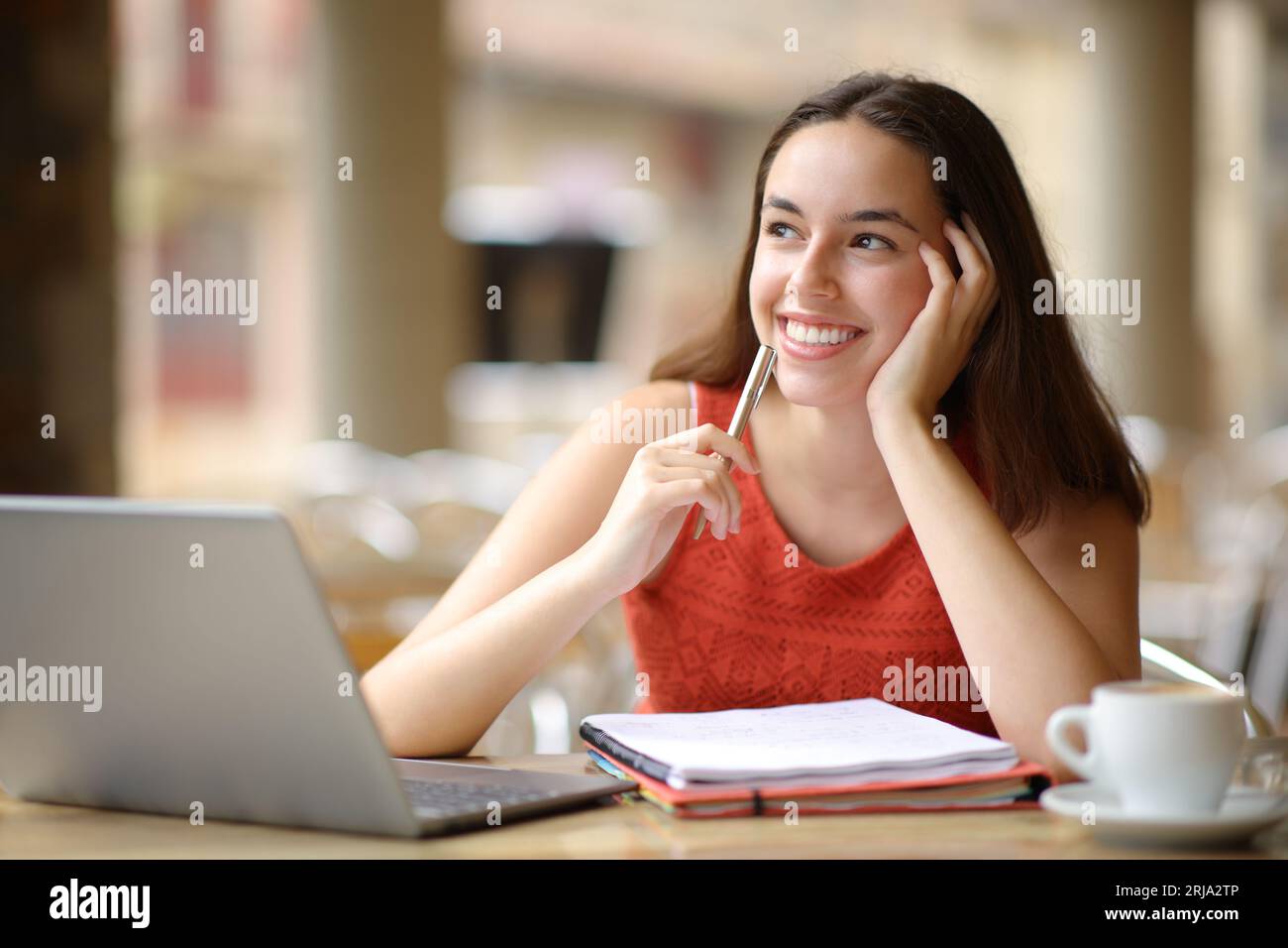 Glücklicher Student mit Laptop und Notebook, der in einer Restaurantterrasse auf Side blickt Stockfoto