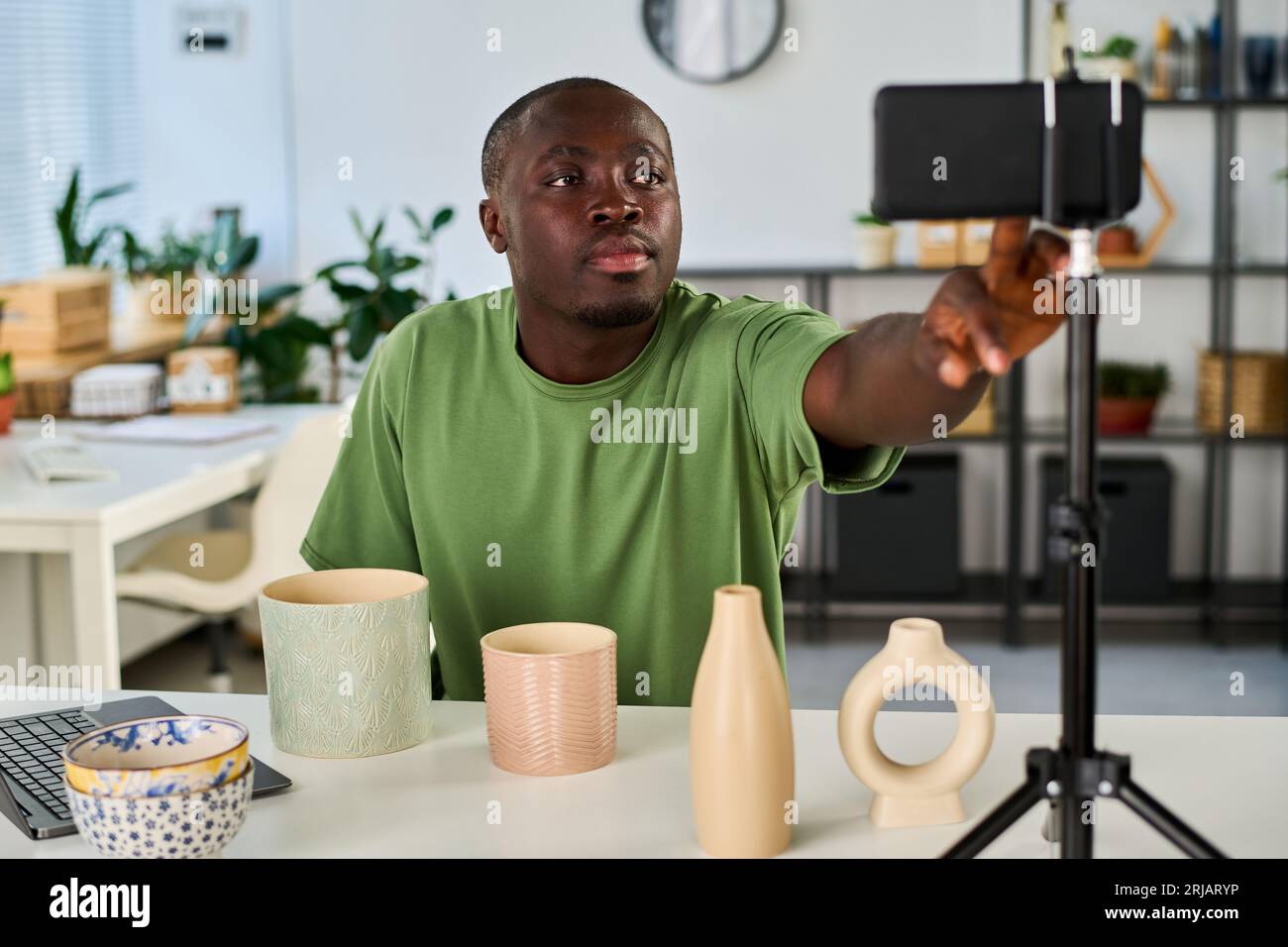 Afroamerikaner beginnt mit der Aufnahme oder dem Livestream, während er mit handgemachten Gegenständen am Schreibtisch sitzt und die Taste auf dem Smartphone-Bildschirm drückt Stockfoto