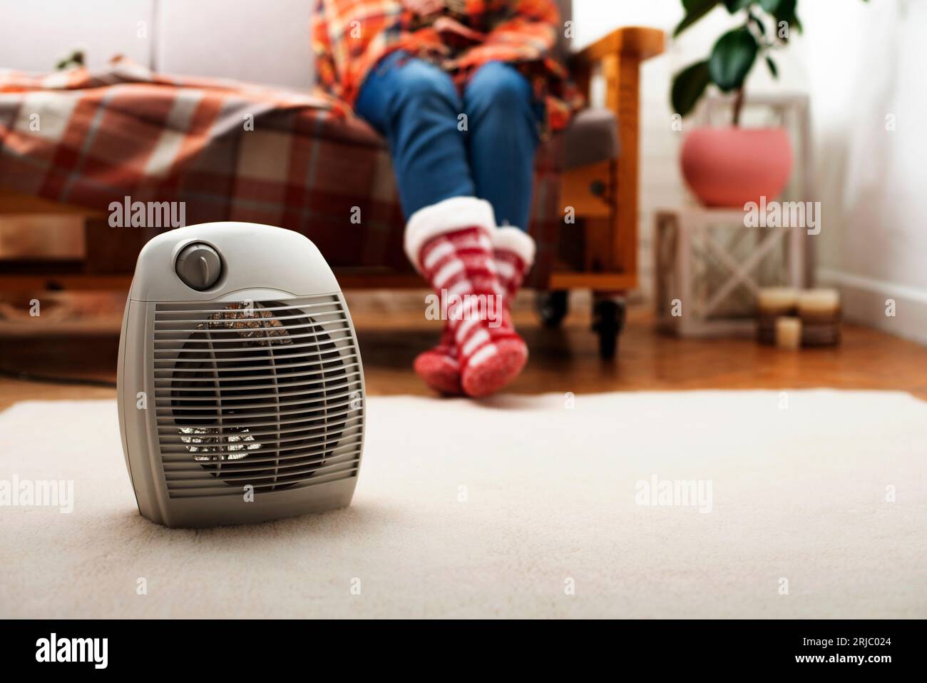 Elektrische Heizung mit Ventilator auf dem Boden im Wohnzimmer mit menschlichem Sitzen auf dem Sofa im Hintergrund Stockfoto