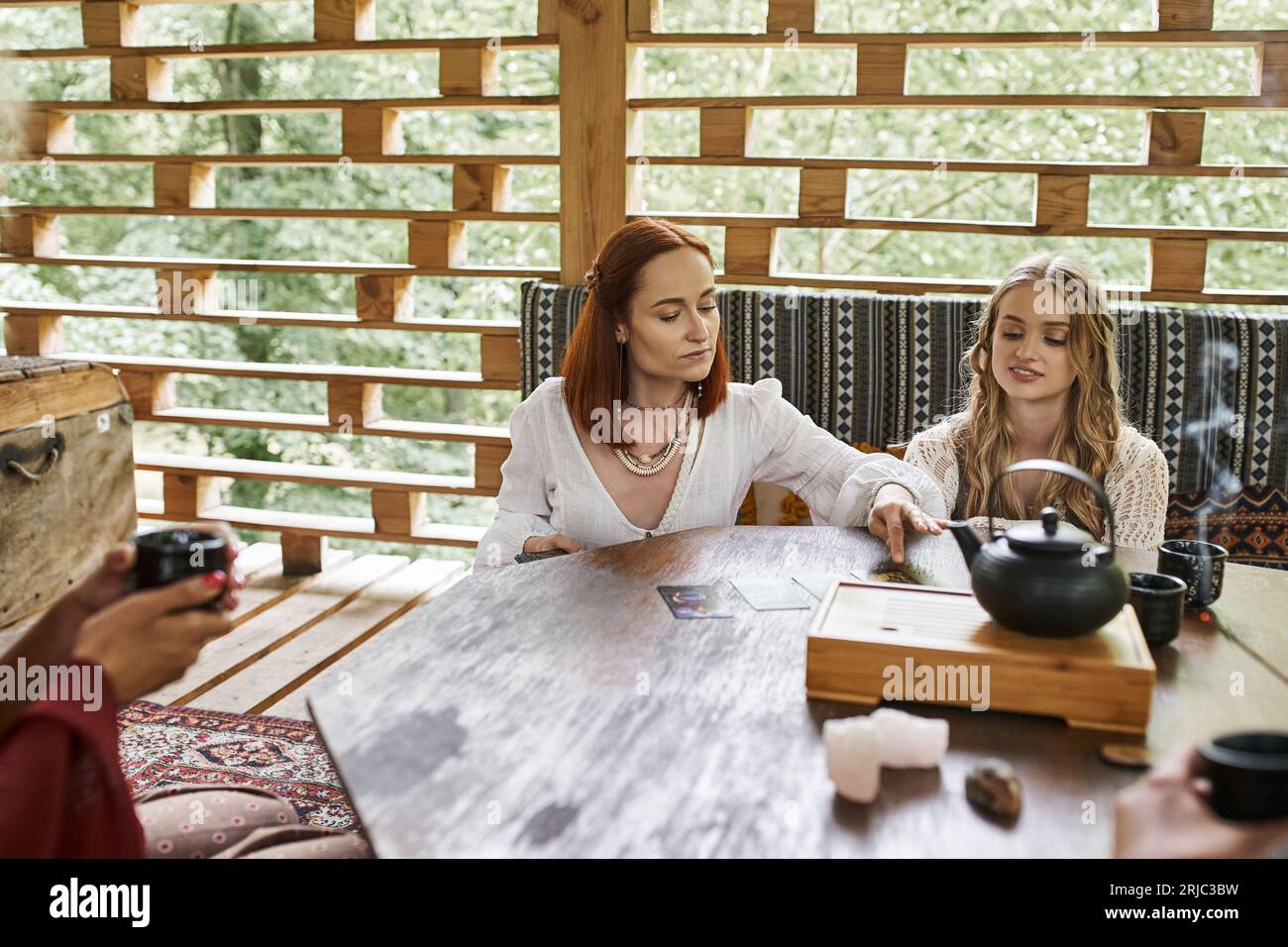 Frau, die Tarotkarten in der Nähe von Freundinnen liest, die am Holztisch sitzen, Harmonie und Ruhe Stockfoto
