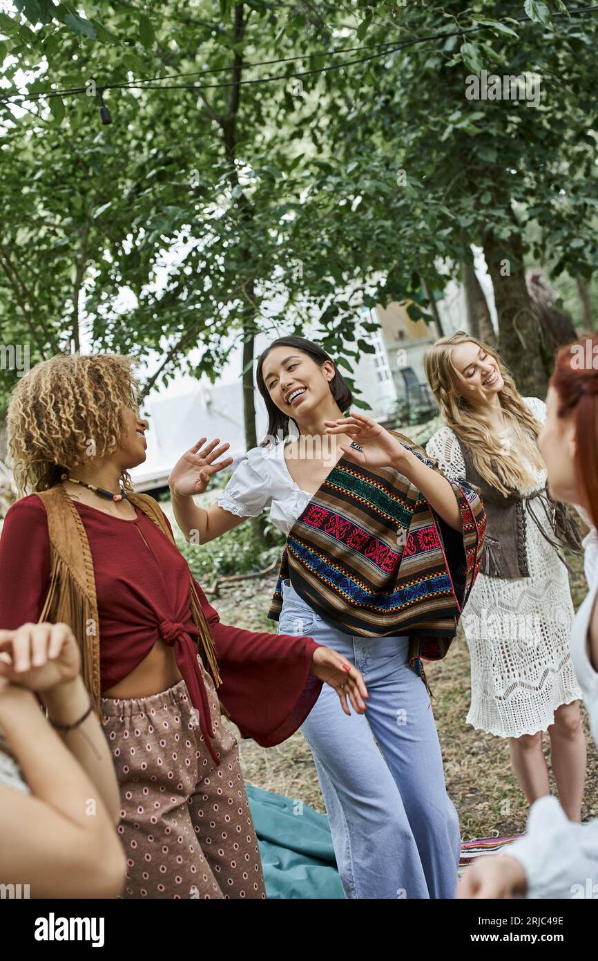 Fröhliche multiethnische Frauen in Boho-Outfits tanzen im Retreat Center zusammen Stockfoto