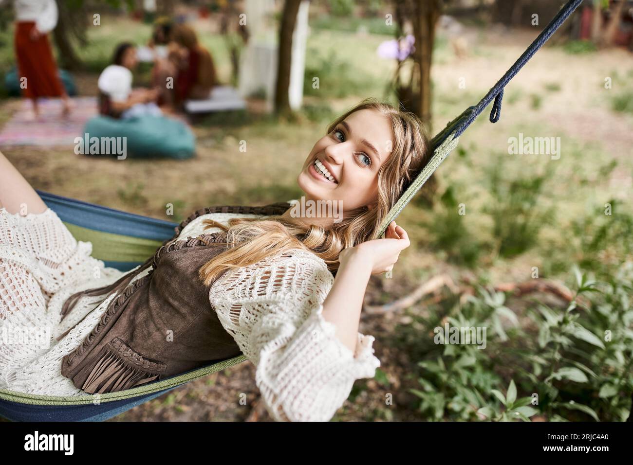 Glückliche junge blonde Frau in Boho-Kleidung, die sich in der Hängematte draußen im Retreat Center entspannt Stockfoto