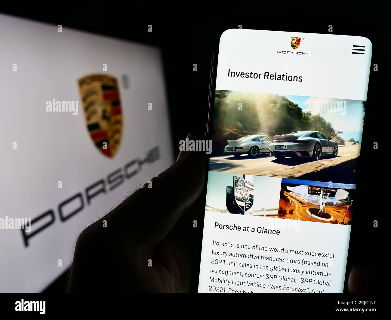 Person, die ein Mobiltelefon hält, mit der Webseite des Automobilunternehmens Dr. Ing. H.c. F. Porsche AG auf dem Bildschirm mit Logo. Konzentrieren Sie sich auf die Mitte der Telefonanzeige. Stockfoto