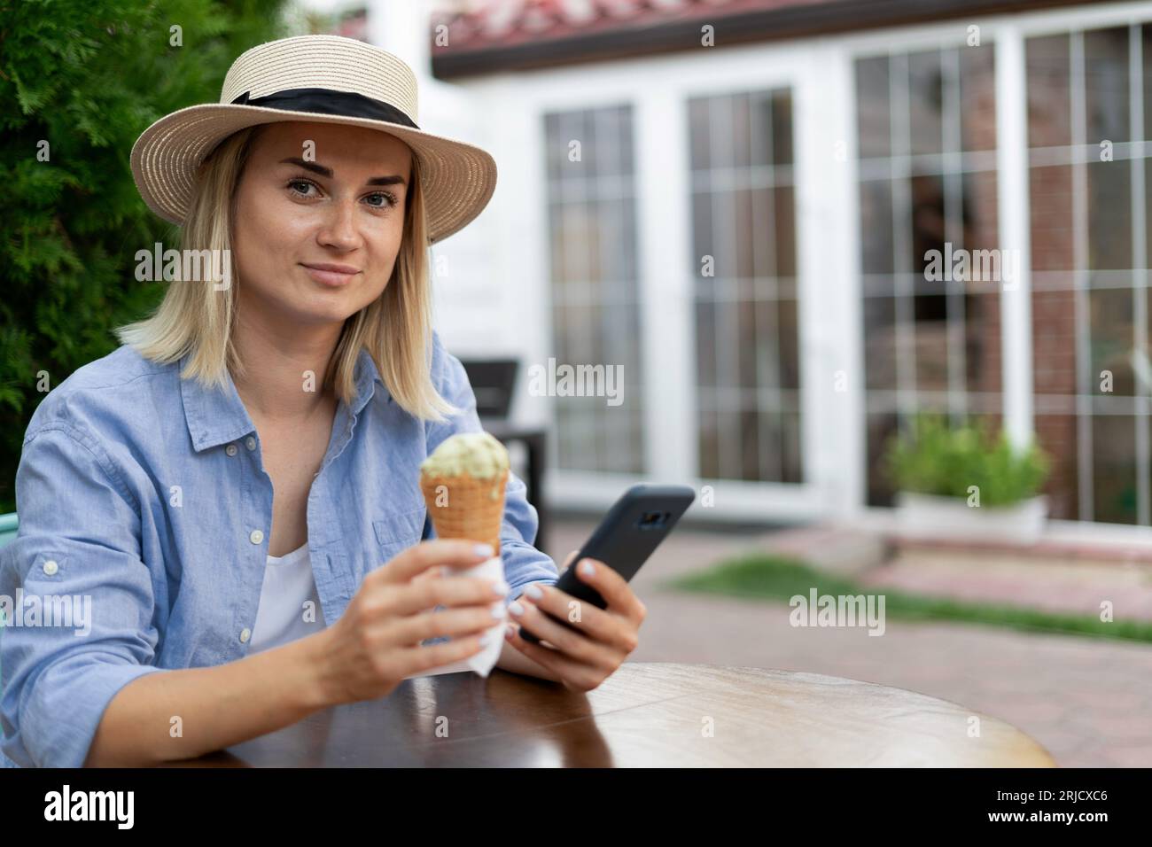 Frau, die Eis mit dem Smartphone im Straßencafé isst. Porträt eines Mädchens mit Eiscreme, das in sozialen Medien oder in Nachrichten im Freien surft Stockfoto