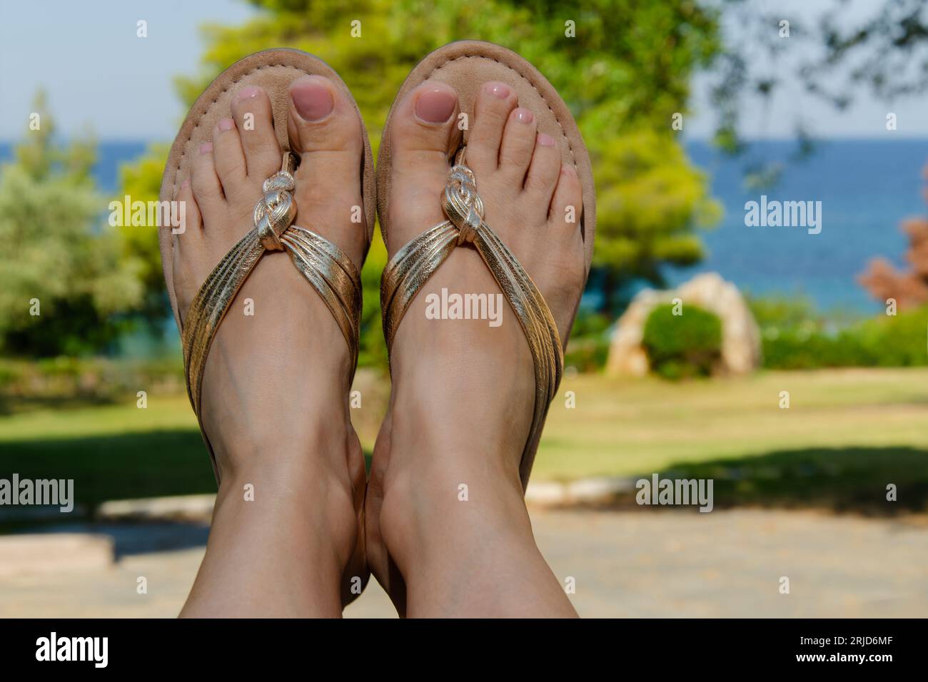 Damenfüße in Sandalen gegen eine Meereslandschaft in Elea Sithonia Halkidiki Griechenland. Zehen. Stockfoto