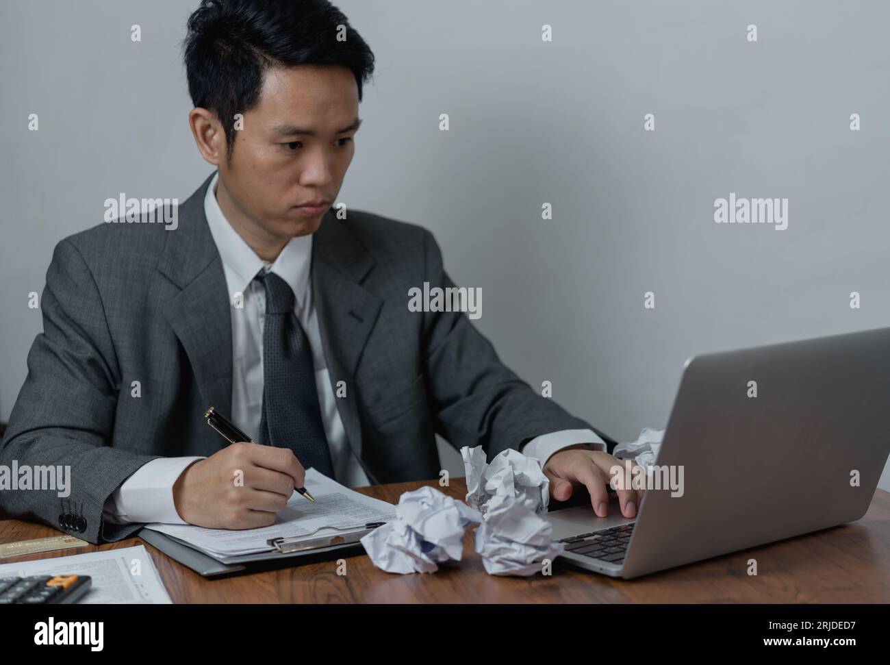 Ein asiatischer Mann, der mit einem Laptop auf dem Schreibtisch arbeitet, konzentrierte sich auf seine Arbeit, mit einem ernsten Gesichtsausdruck. Stockfoto