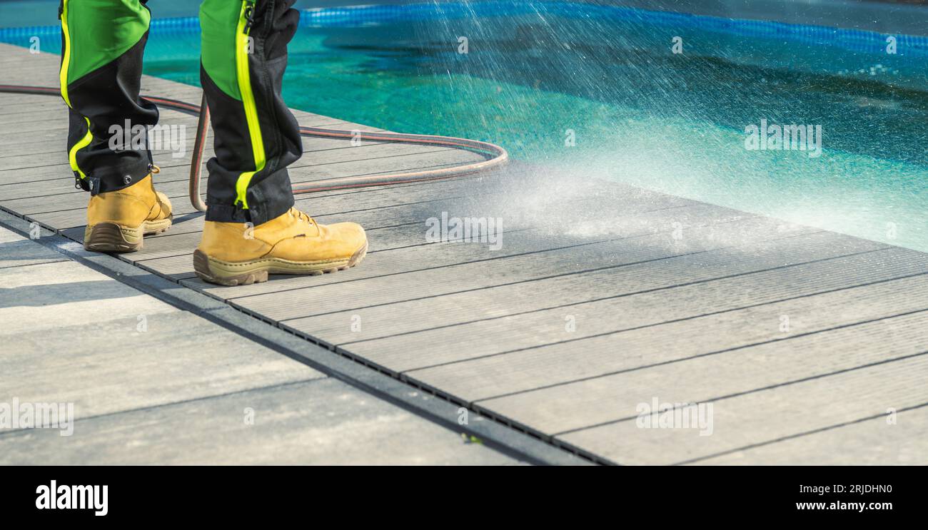 Mann, der sein Poolside Deck mit Wasser putzt. Wartung Des Schwimmbadbereichs. Stockfoto