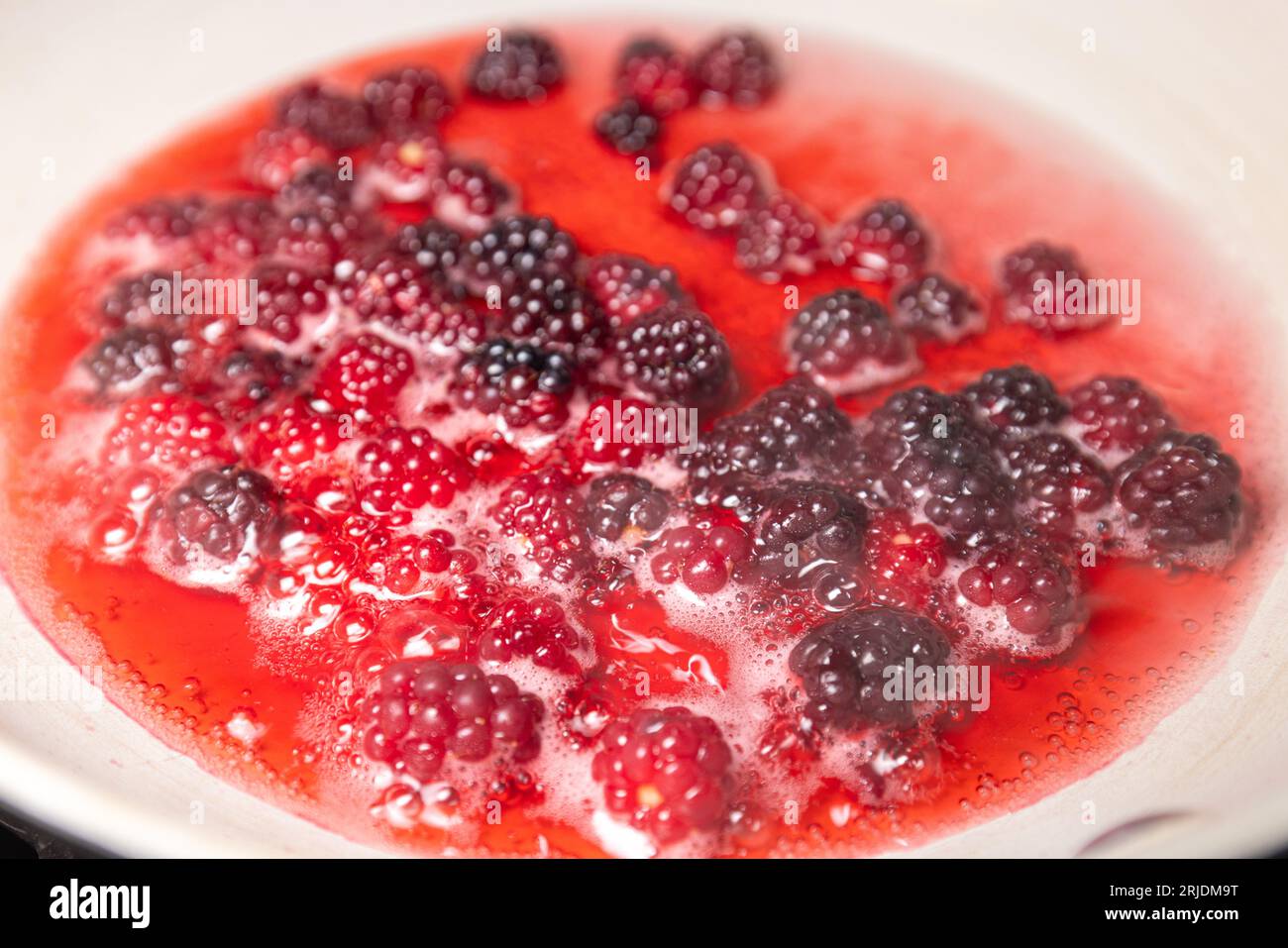 Nahaufnahme eines Haufens frisch gepflückter Waldbeeren, die in einer Pfanne mit etwas Wasser und Zucker kochen Stockfoto