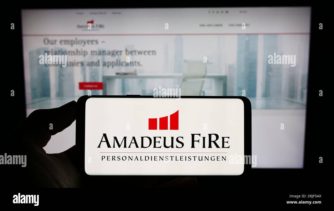 Person, die ein Mobiltelefon mit dem Logo des deutschen Personalvermittlungsunternehmens Amadeus Fire AG auf dem Bildschirm vor der Geschäftswebseite hält. Konzentrieren Sie sich auf das Display des Telefons. Stockfoto