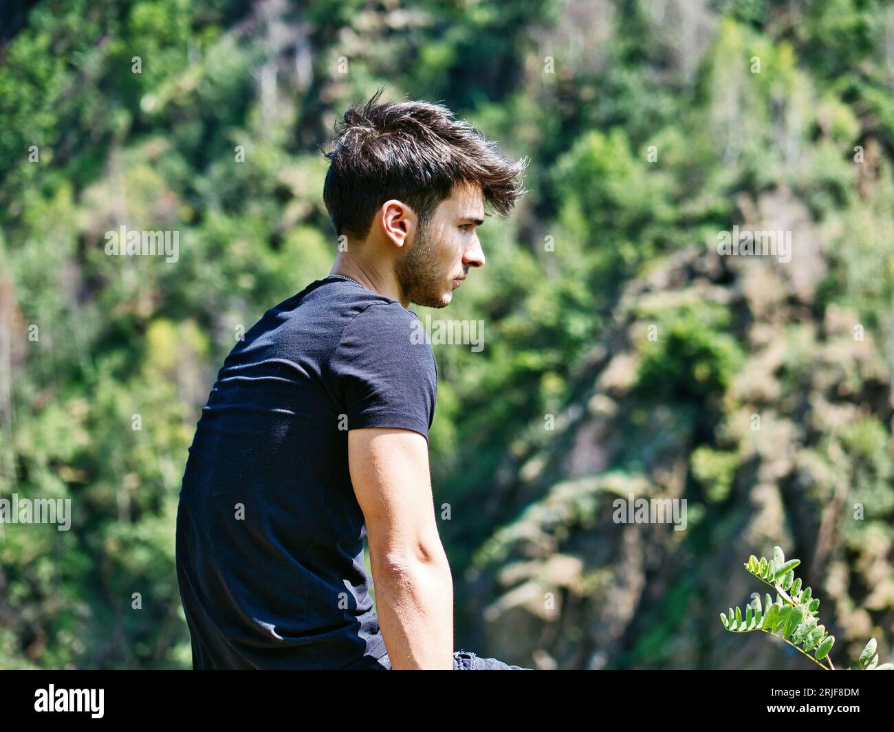 Foto eines Mannes, der auf einem Felsen sitzt und die Aussicht betrachtet Stockfoto