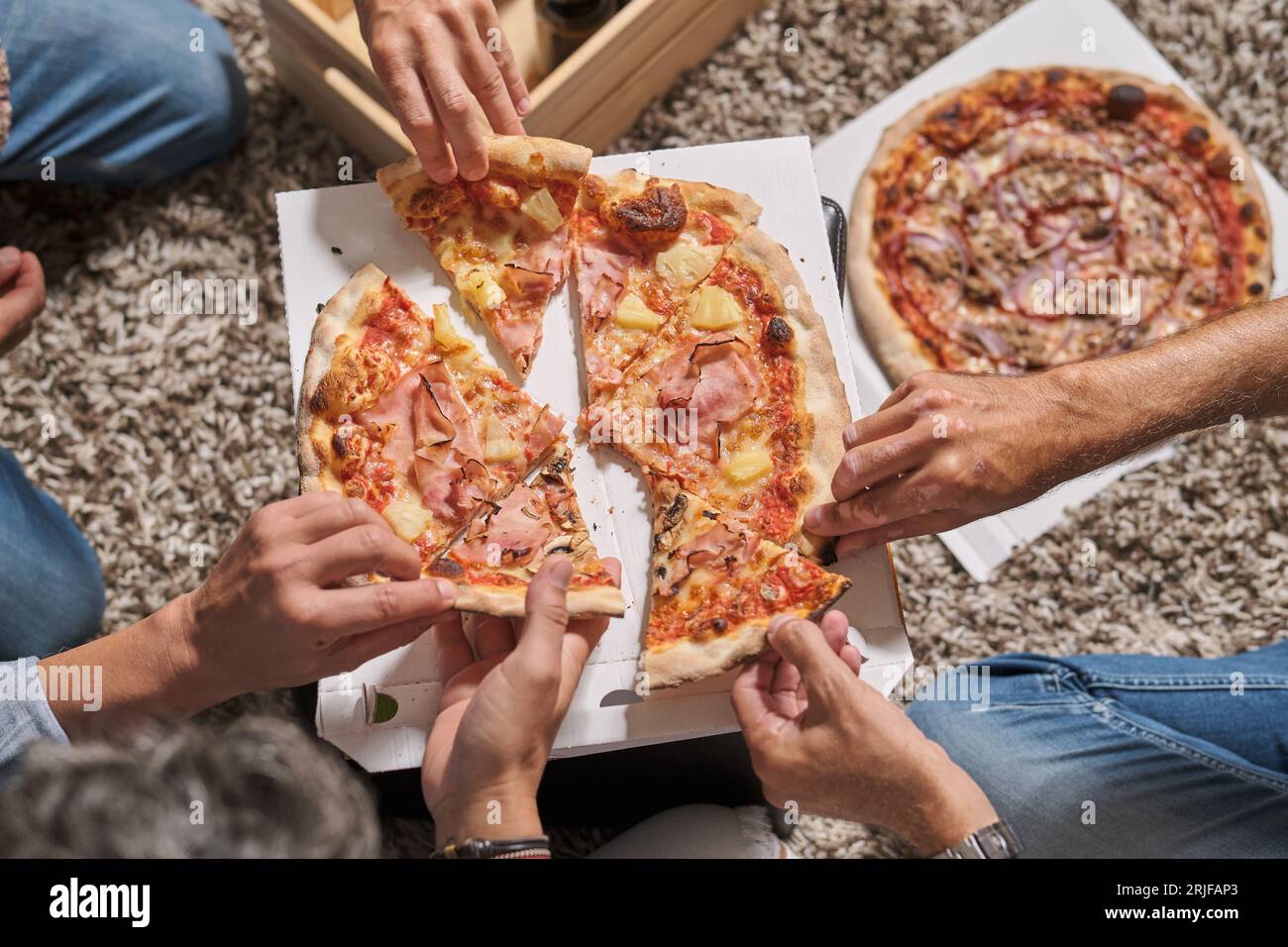 Von oben gesichtslose männliche Freunde, die sich treffen und köstliche Pizzascheiben nehmen, während sie gemeinsam am Wochenende feiern Stockfoto