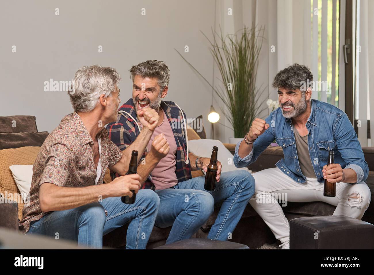 Begeisterte reife männliche Fans mit Flaschen Bier, die gemeinsam Spaß haben und den Sieg während des Spiels im Wohnzimmer zu Hause feiern Stockfoto