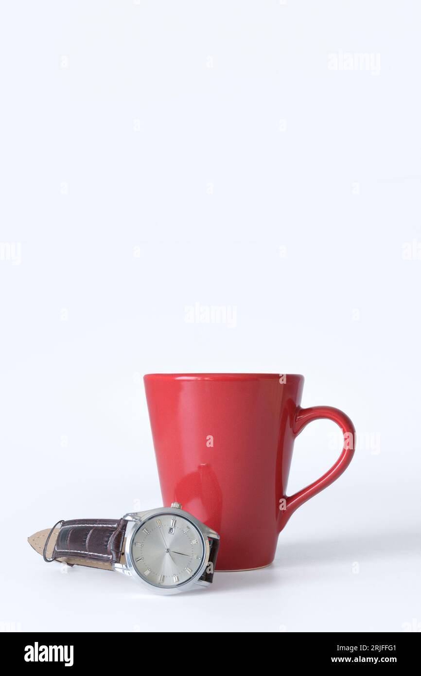 Roter Becher und Armbanduhr auf einem Armband auf weißem Hintergrund. modell, Banner vertikal. Konzept der Kaffeezeit Stockfoto