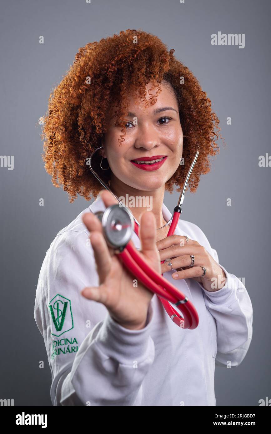 Tierärztin, hübsch mit rotem Haar, zeigt der Kamera ein Stethoskop in weißer Uniform. Isoliert auf grauem Hintergrund. Stockfoto