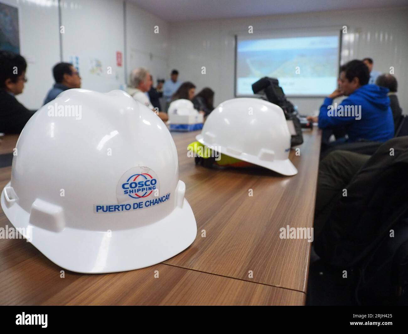 Der Helm des Auftragnehmers befindet sich im Besprechungsraum der Hafenanlagen von Chancay, die an der peruanischen Küste, 60 km nördlich von Lima, noch im Bau sind. Der Hafen von Chancay wäre das Drehkreuz des südamerikanischen Pazifiks mit der Kapazität, drei E-Schiffe aufzunehmen, die zwischen 18.000 und 24.000 Container beladen können, weshalb er als Tor des direkten Seeverkehrs von Südamerika nach Asien und Ozeanien gilt. Der Hafen wird in einem Joint Venture von Cosco Shipping aus China gebaut Stockfoto Der Helm des Auftragnehmers befindet sich im Besprechungsraum der Hafenanlagen von Chancay, die an der peruanischen Küste, 60 km nördlich von Lima, noch im Bau sind. Der Hafen von Chancay wäre das Drehkreuz des südamerikanischen Pazifiks mit der Kapazität, drei E-Schiffe aufzunehmen, die zwischen 18.000 und 24.000 Container beladen können, weshalb er als Tor des direkten Seeverkehrs von Südamerika nach Asien und Ozeanien gilt. Der Hafen wird in einem Joint Venture von Cosco Shipping aus China gebaut Stockfoto
