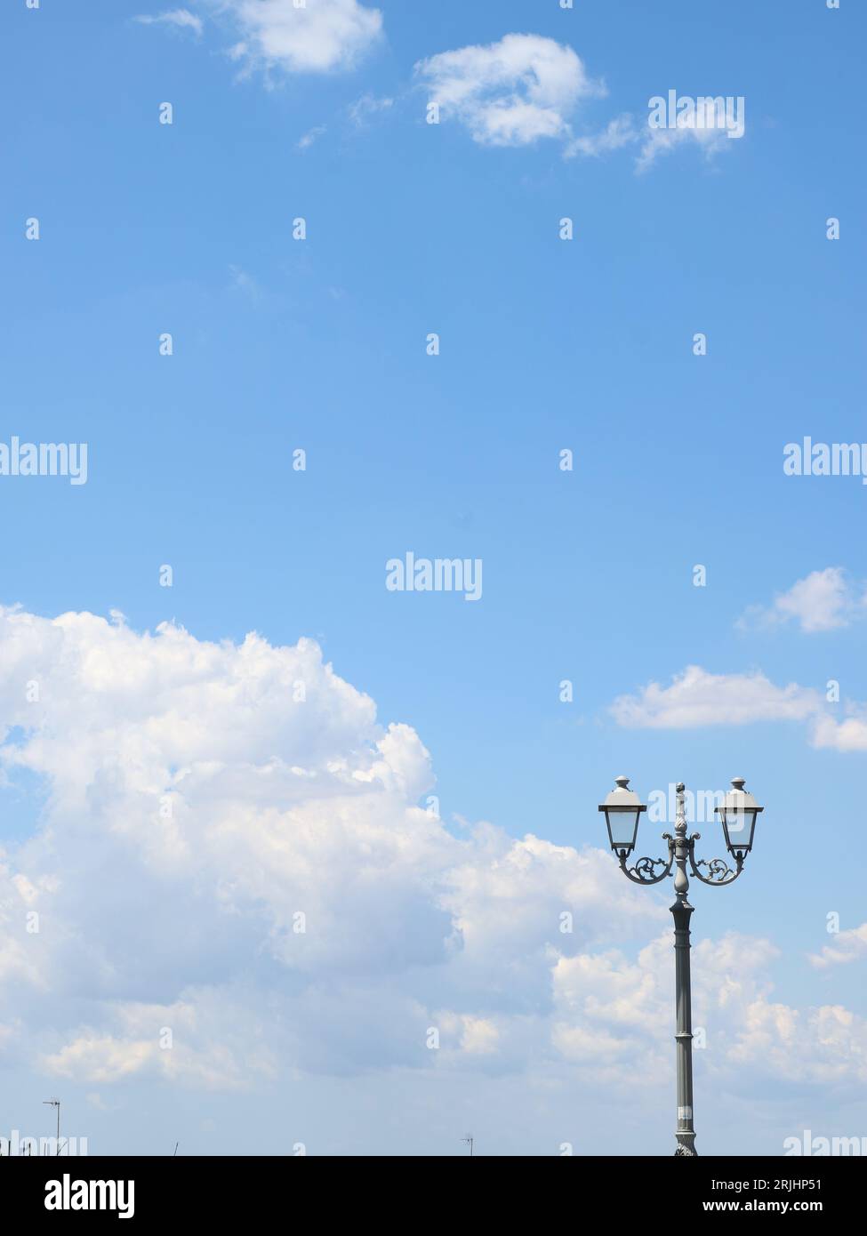 Lampione con due lampadine che si staglia nel cielo azzurro con qualche nuvola bianca al mattino. Straßenlaterne am hellen Himmel mit weißen Wolken Stockfoto