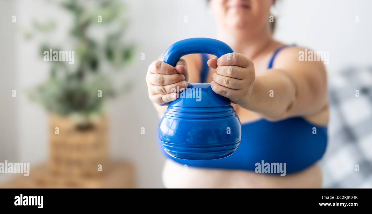 Plus Größe Frau, die Übungen mit Kurzhanteln macht, ihren Körper im Wohnzimmer stärkt, selektive Fokussierung. Stockfoto