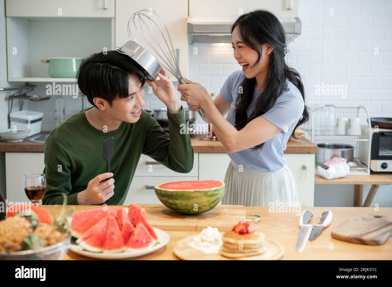 Ein hübsches und verspieltes junges asiatisches Paar tut so, als kämpft es mit Utensilien und hat Spaß beim Zubereiten von Speisen in der Küche. Lustige Kuppeln Stockfoto