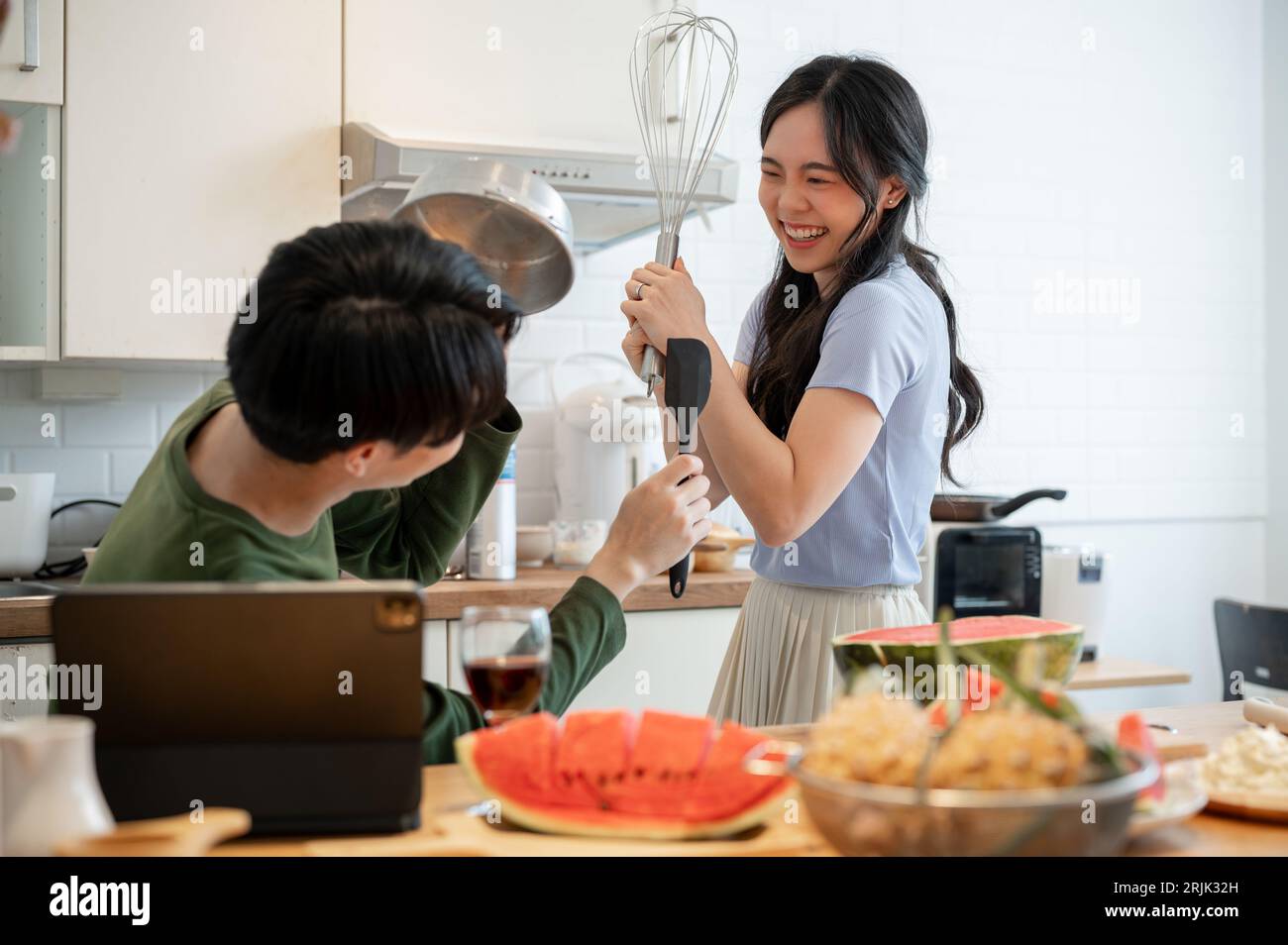 Ein hübsches und verspieltes junges asiatisches Paar tut so, als kämpft es mit Utensilien und hat Spaß beim Zubereiten von Speisen in der Küche. Lustige Kuppeln Stockfoto