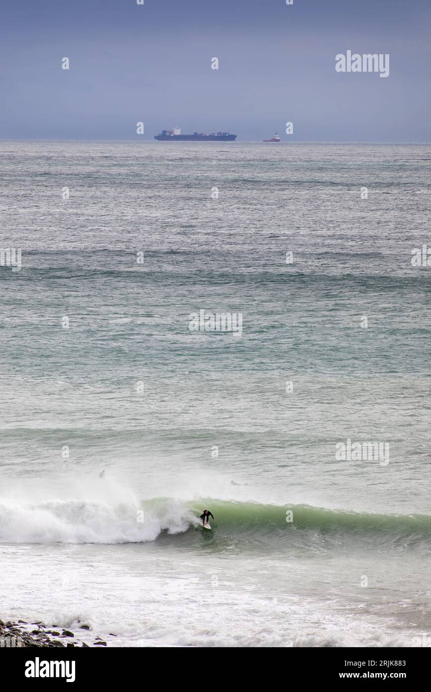 Bild von Tim Cuff - 20. Mai 2023 - Ein Surfer macht das Beste aus dem großen Anstieg in Cable Bay. Das schlechte Wetter brachte das kaputte Schiff Shiling ins Sichtfeld Stockfoto