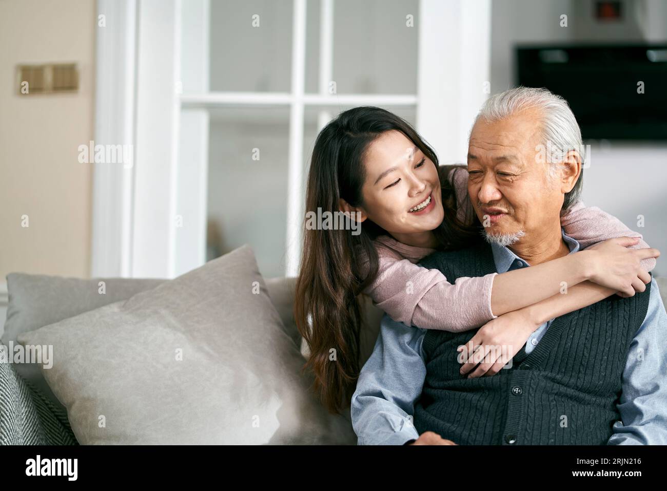 asiatischer Seniorenvater und Erwachsene Tochter, die zu Hause auf der Couch sitzen und ein angenehmes Gespräch genießen Stockfoto