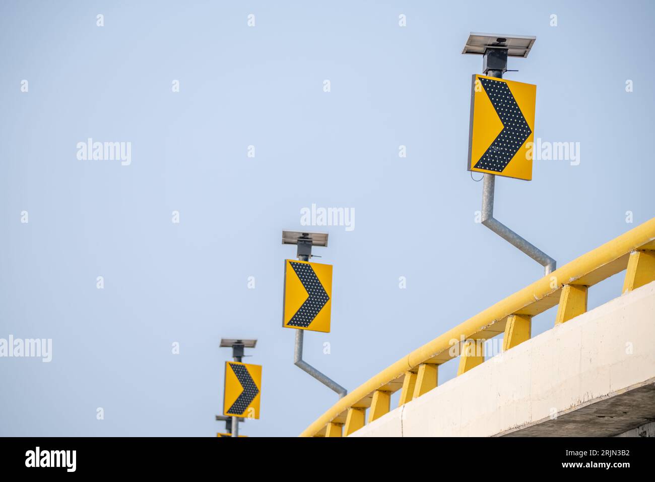 Gelbe Verkehrsschilder führen den Fahrer auf kurvenförmigen Straßen. Symbole sorgen für Sicherheit, wenn sie unter dem wachsamen blauen Himmel durch die Straßen navigieren. Pfeilzeichen Stockfoto