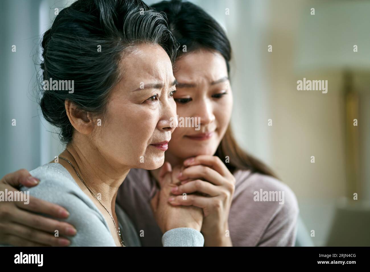 Traurige asiatische Seniormutter und erwachsene Tochter, die Hände hält Stockfoto