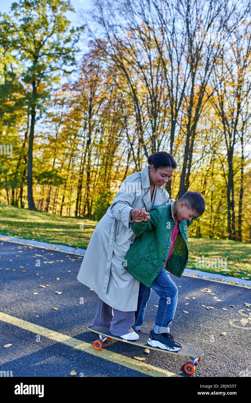 Mutter und Sohn, Bindungszeit, Herbstpark, afroamerikanische Frau, die in der Nähe von Boy auf Penny Board läuft Stockfoto