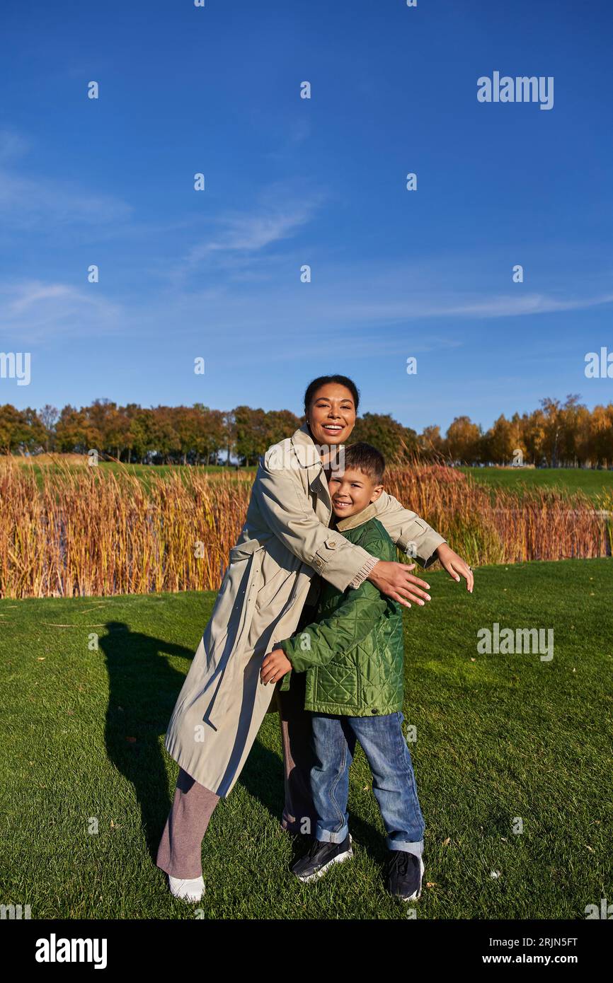 Binding, herbstliche Natur, glückliche afroamerikanische Mutter, die Sohn umgibt, Familie in Oberbekleidung, Herbst Stockfoto