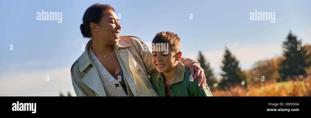 Positive afroamerikanische Mutter umarmt sich mit Sohn, Herbstsaison, Oberbekleidung, Familienbindung, Banner Stockfoto