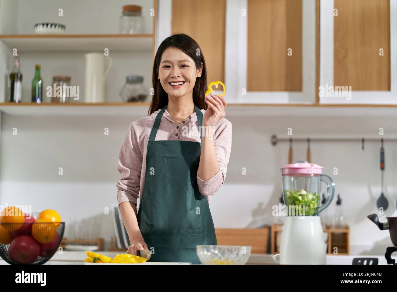 Glückliche junge asiatische Hausfrau, die in der Küche steht und die Kamera lächelt Stockfoto