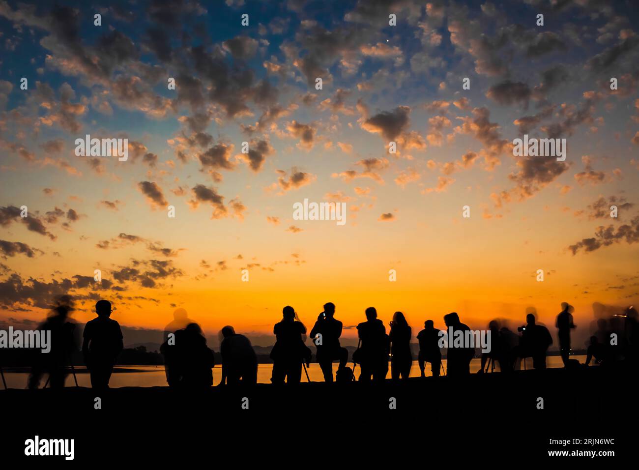 Ein Langzeitbelichtungsbild eines lebhaften Sonnenuntergangs beleuchtet eine ruhige Landschaft mit einer Gruppe von Menschen, die am Horizont silhouettiert sind Stockfoto