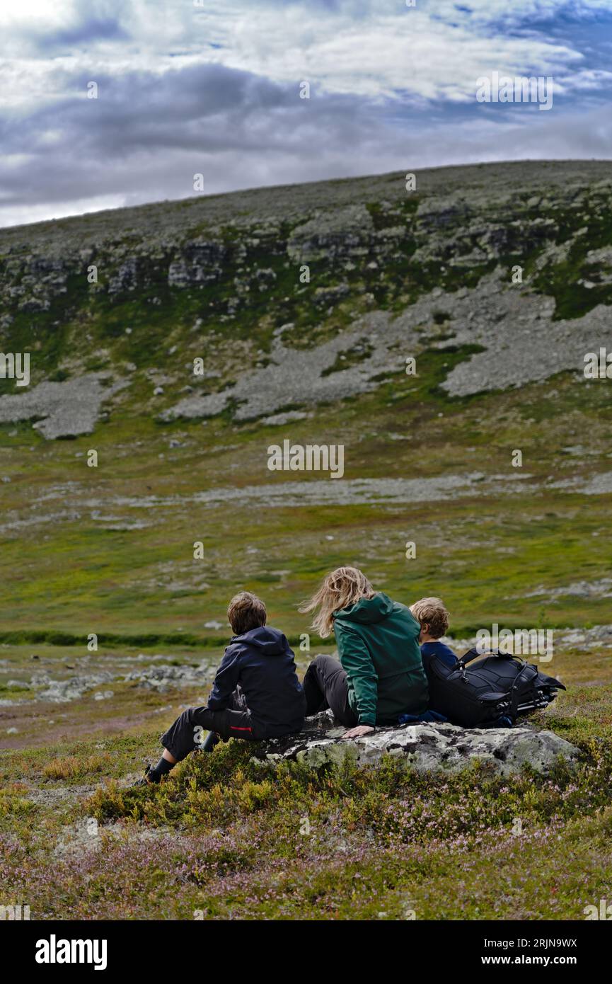 Alleinerziehende Mutter sitzt mit ihren Kindern auf einem Felsen und genießt den Blick auf die Bergklippen in der Tundra-Landschaft Schwedens. Gesunde Lebensweise Familie in der Natur t Stockfoto