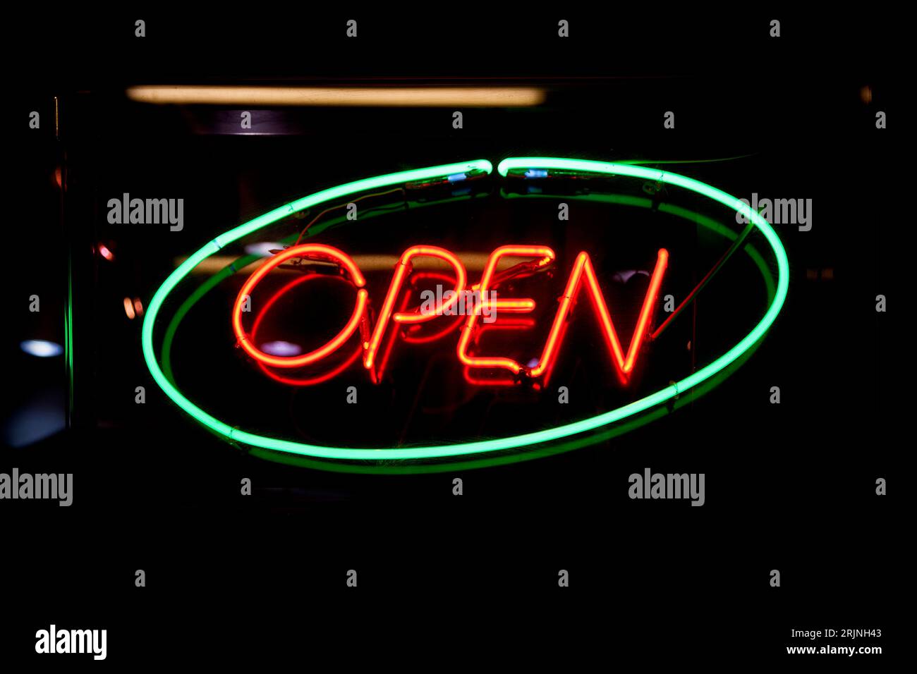 Nahaufnahme eines Neonlichts, das in ein grünes Oval geformt ist und das Wort „Open“ (offen) innen rot geschrieben ist. Stockfoto