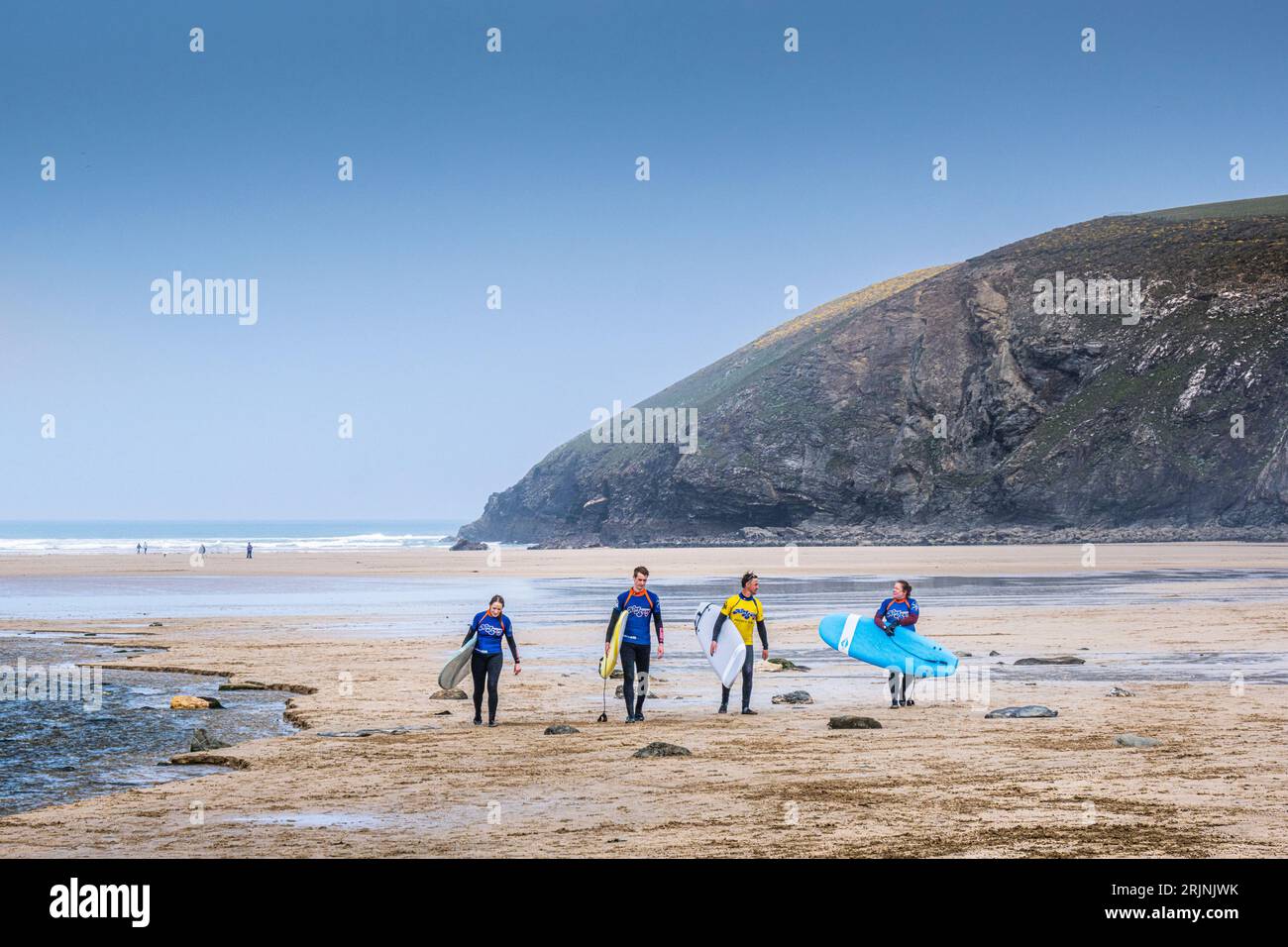 Drei Surfanfänger und ihr Surflehrer tragen ihre Surfbretter nach einem Surfunterricht im Mawgan Porth in Cornwall, Großbritannien. Stockfoto