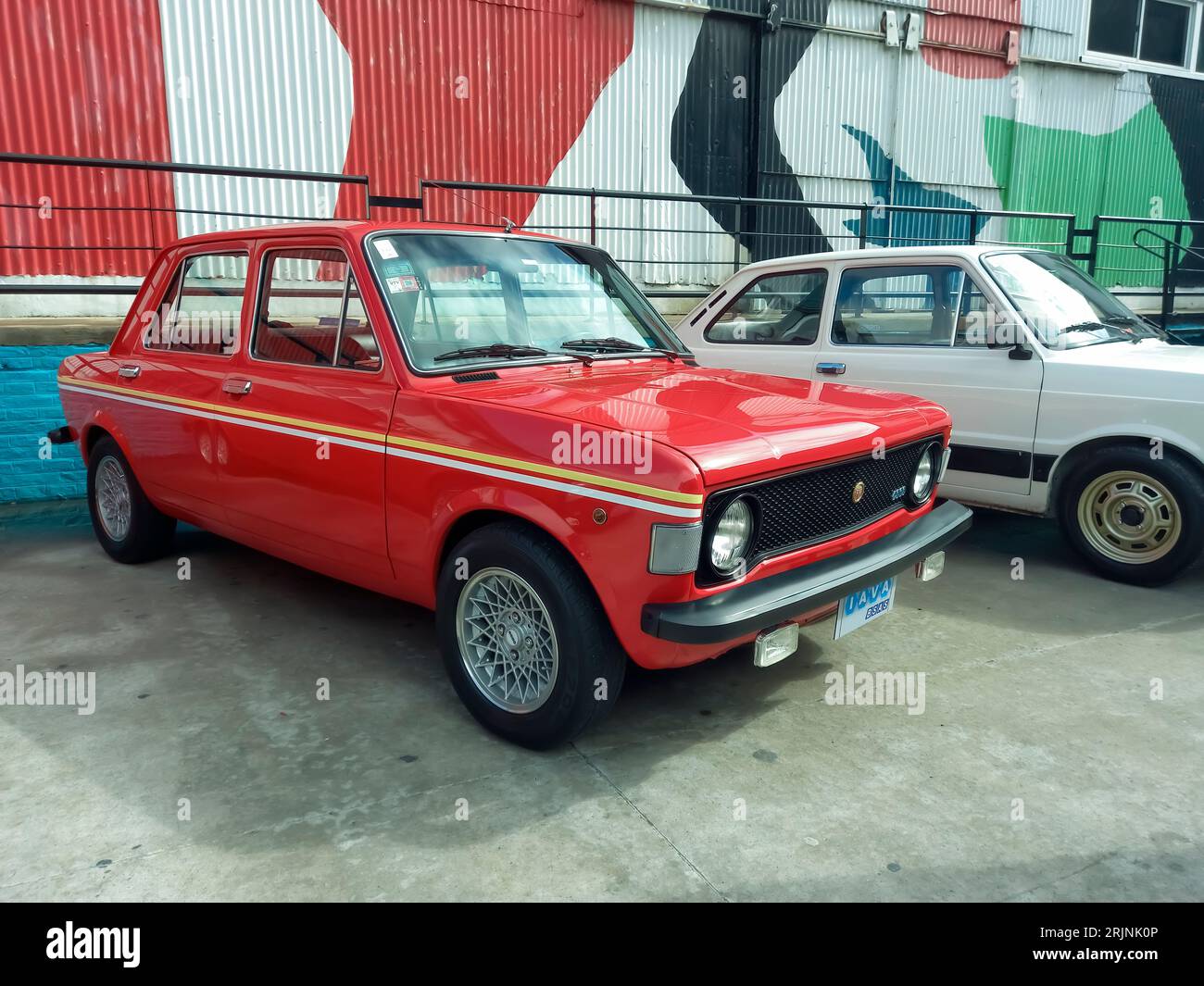 Alte rote Fiat 128 IAVA-Limousine aus den 1970er Jahren, gebaut in Argentinien mit einem farbenfrohen industriellen Hintergrund. Expo Fierro 2023 Oldtimer-Ausstellung. Stockfoto