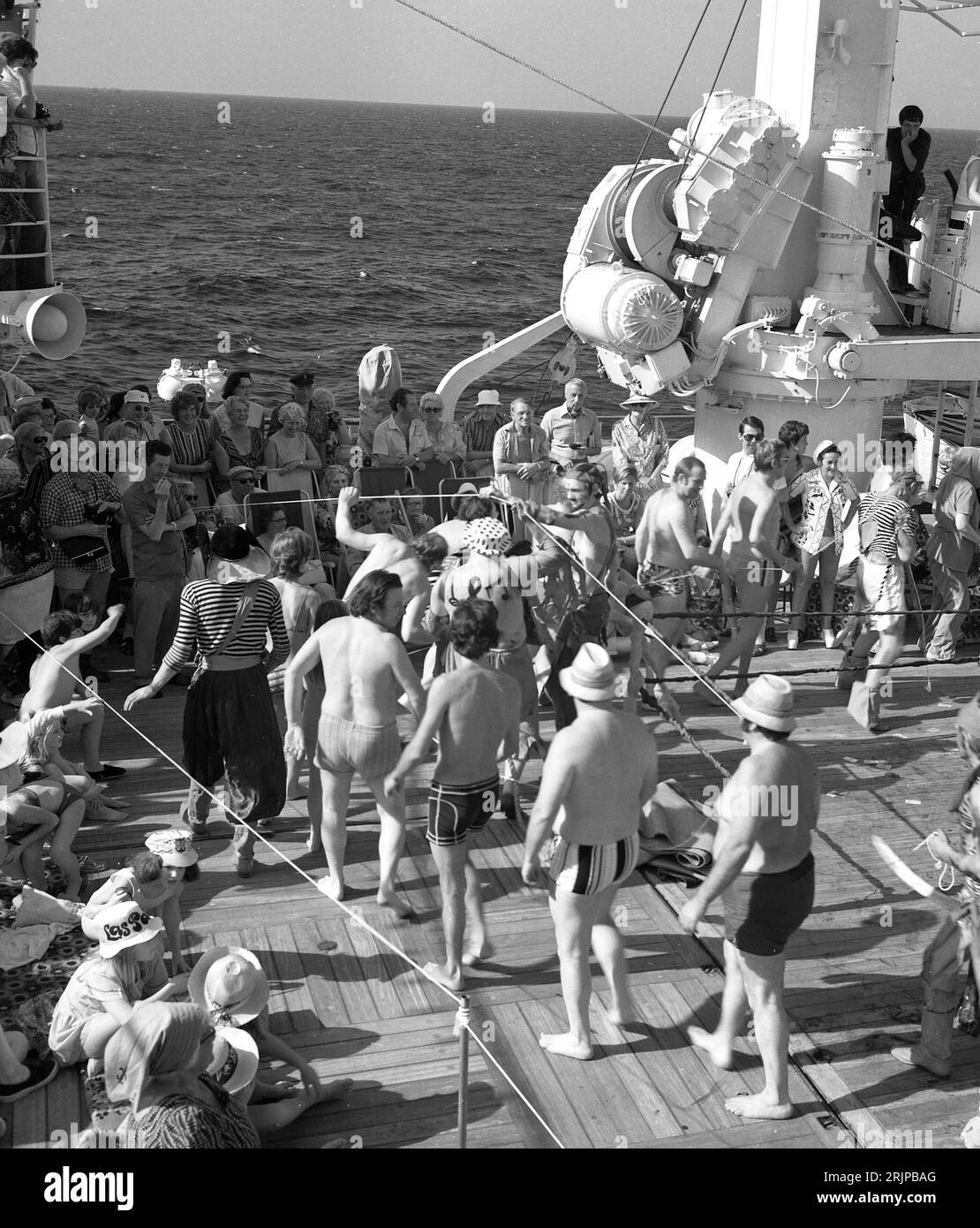 Um die späten 1960er Jahre, historische Passagiere auf dem Deck eines Kreuzfahrtschiffes, die Spaß haben, an der Zeremonie teilzunehmen, wenn ihr Kreuzfahrtschiff den Äquator überquert, während andere Passagiere beobachten. Die Zeremonie „Überquerung der Linie“ oder „Seetaufe“ ist eine der bekanntesten Traditionen, wenn ein Schiff den Äquator überquert. Stockfoto