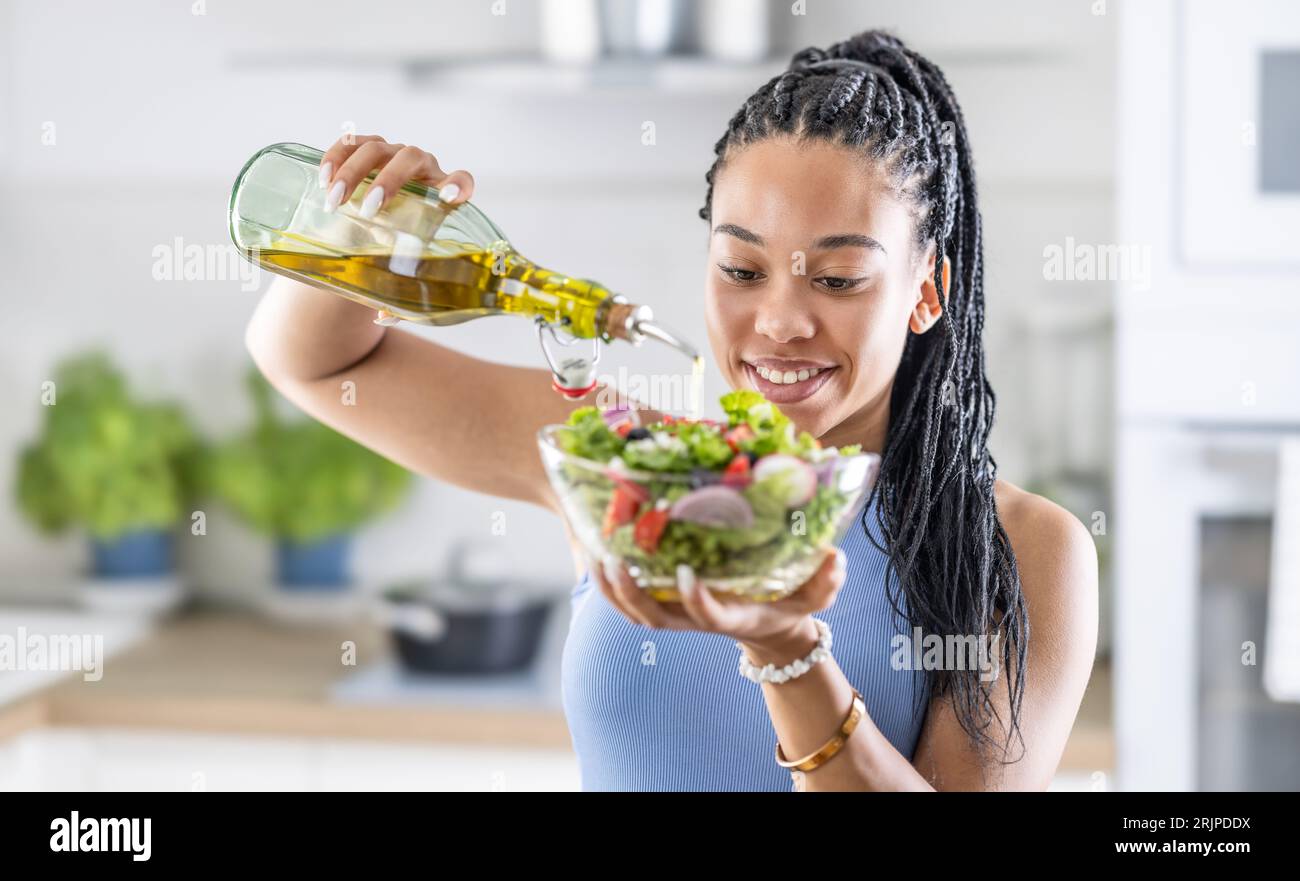 Eine junge afroamerikanische Frau bereitet einen gesunden Blattsalat zu, den sie mit Olivenöl vergießt. Stockfoto