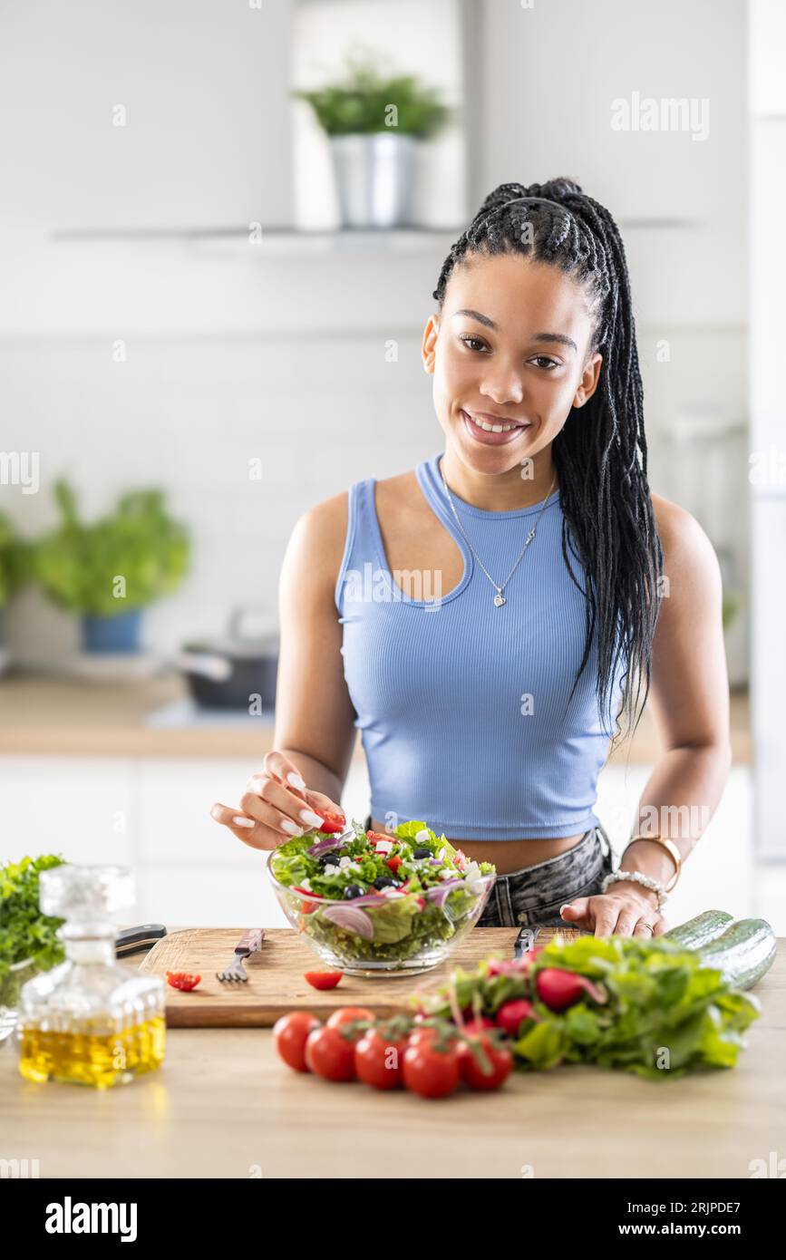 Junge afroamerikanische Frau bereitet gesunden Salat zu, fügt Tomaten hinzu. Stockfoto