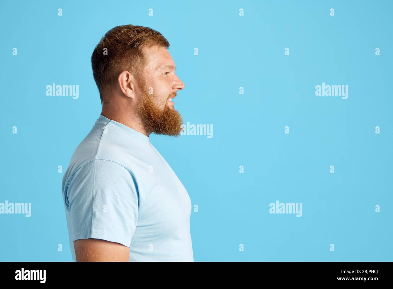 Profil, Seitenansicht eines bärtigen Mannes in einem lässigen weißen T-Shirt, das gerade vor blauem Studiohintergrund aussieht Stockfoto
